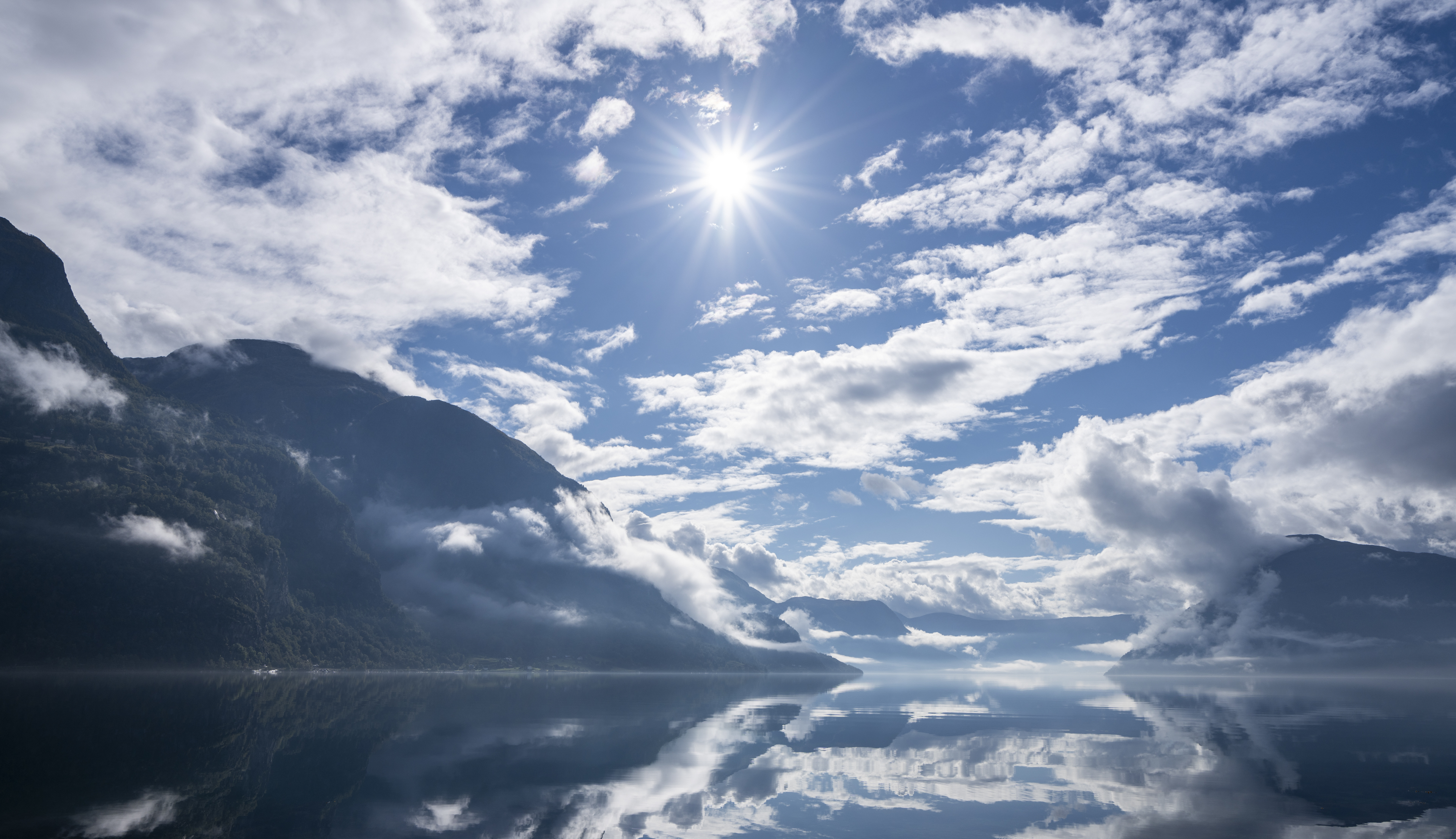 blank fjord omkransa av fjell med flekkvis snø 