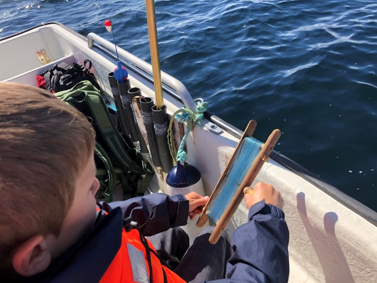Gutt som fisker over ripa  på ein båt med snøre