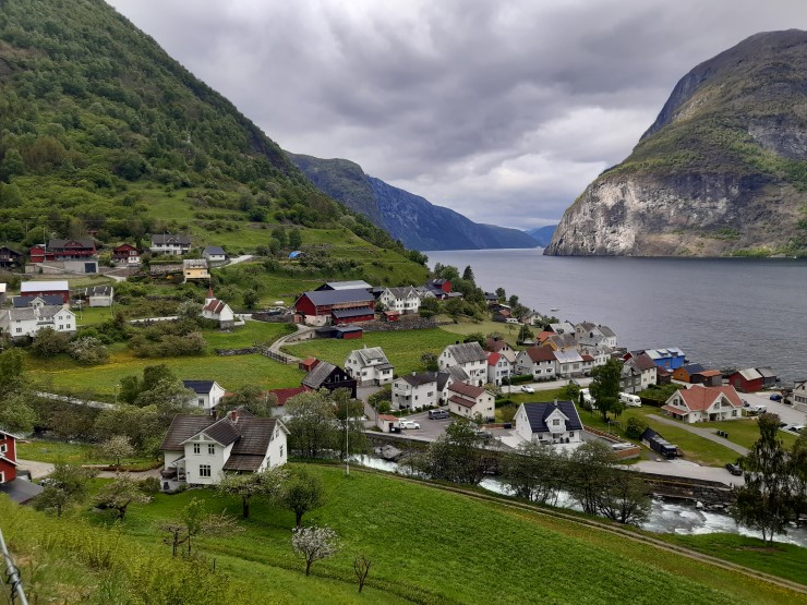 Fjell, grå himmel, fjord, hus og fjøs, elv, grønne lier