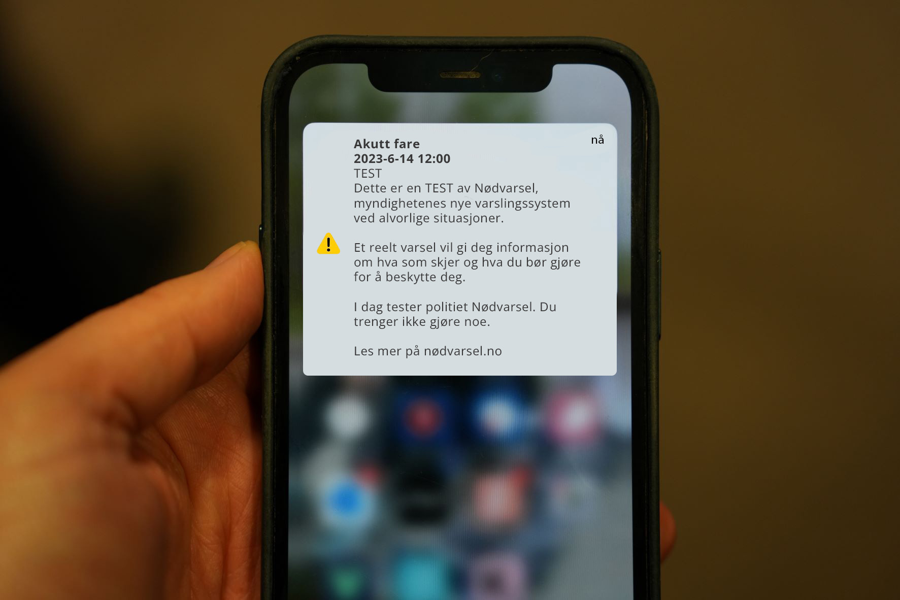 Bildet viser en hånd som holder en mobiltelefonen. På skjermen vises et varsel med tekst og en illustrasjon av et utropstegn. 