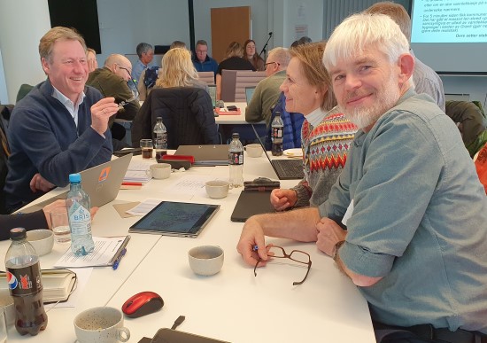 Personer rundt et bord som deltar på konferanse.