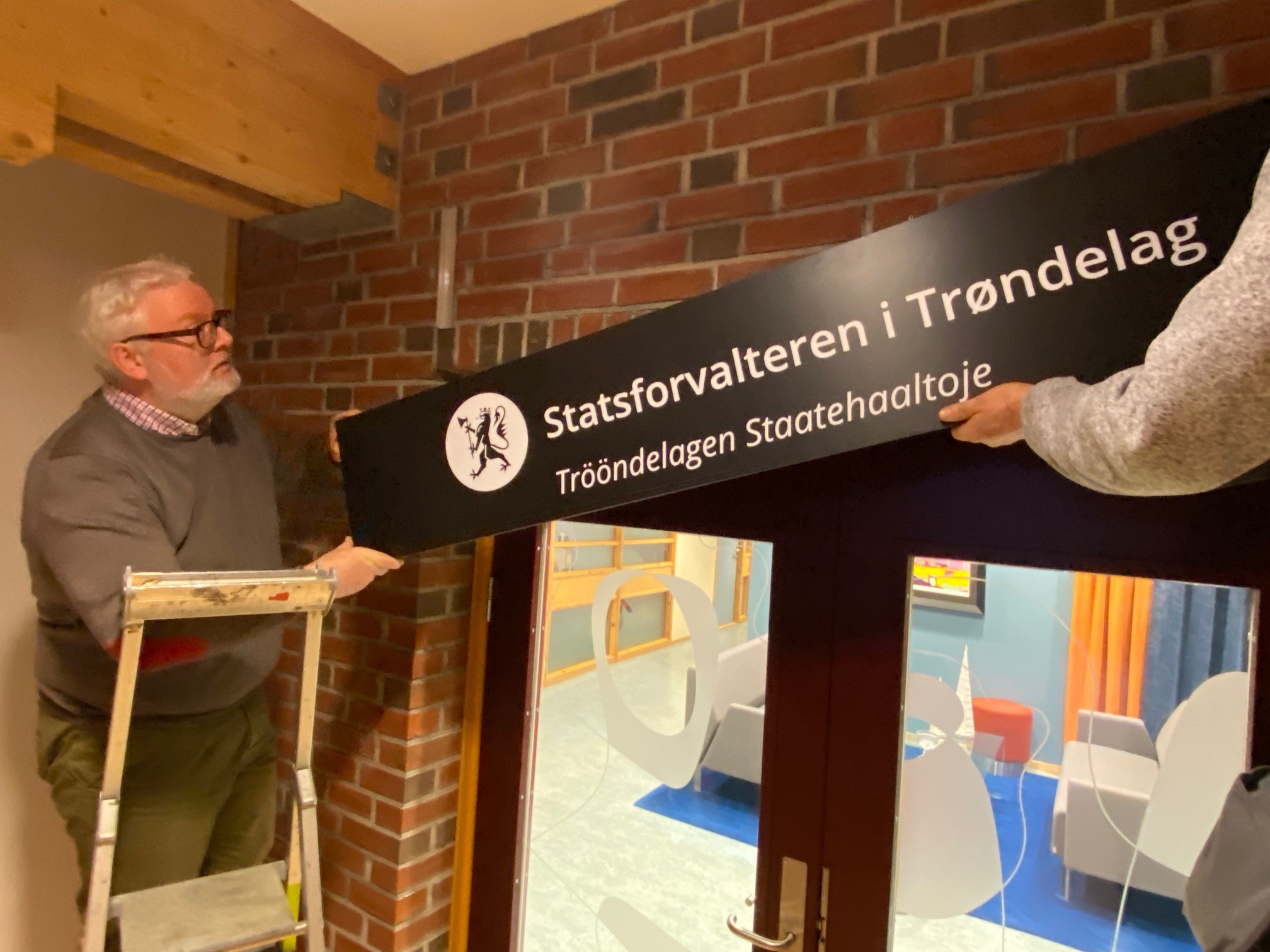 Statsforvalter Frank Jenssen hjalp til da skiltene til Statsforvalteren i Trøndelag ble hengt opp utenfor lokalene i Statens Hus på Steinkjer. 