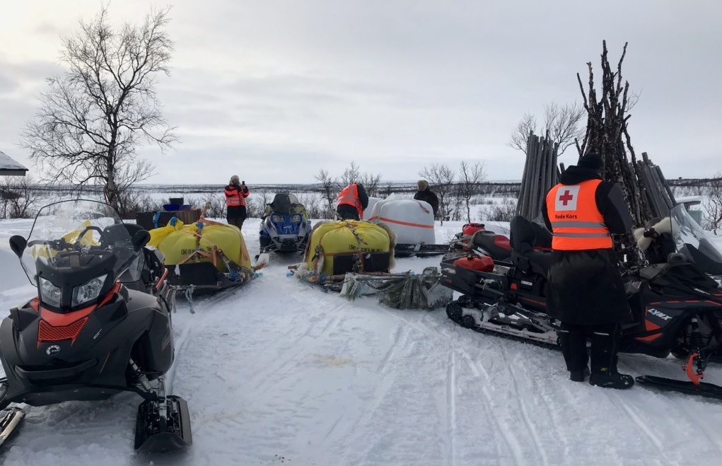 Mannskap fra Røde Kors og flere skutere med sleder lastet med nødfôr, 