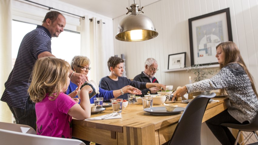 Seks personer i forskjellig alder samlet rundt middagsbord.