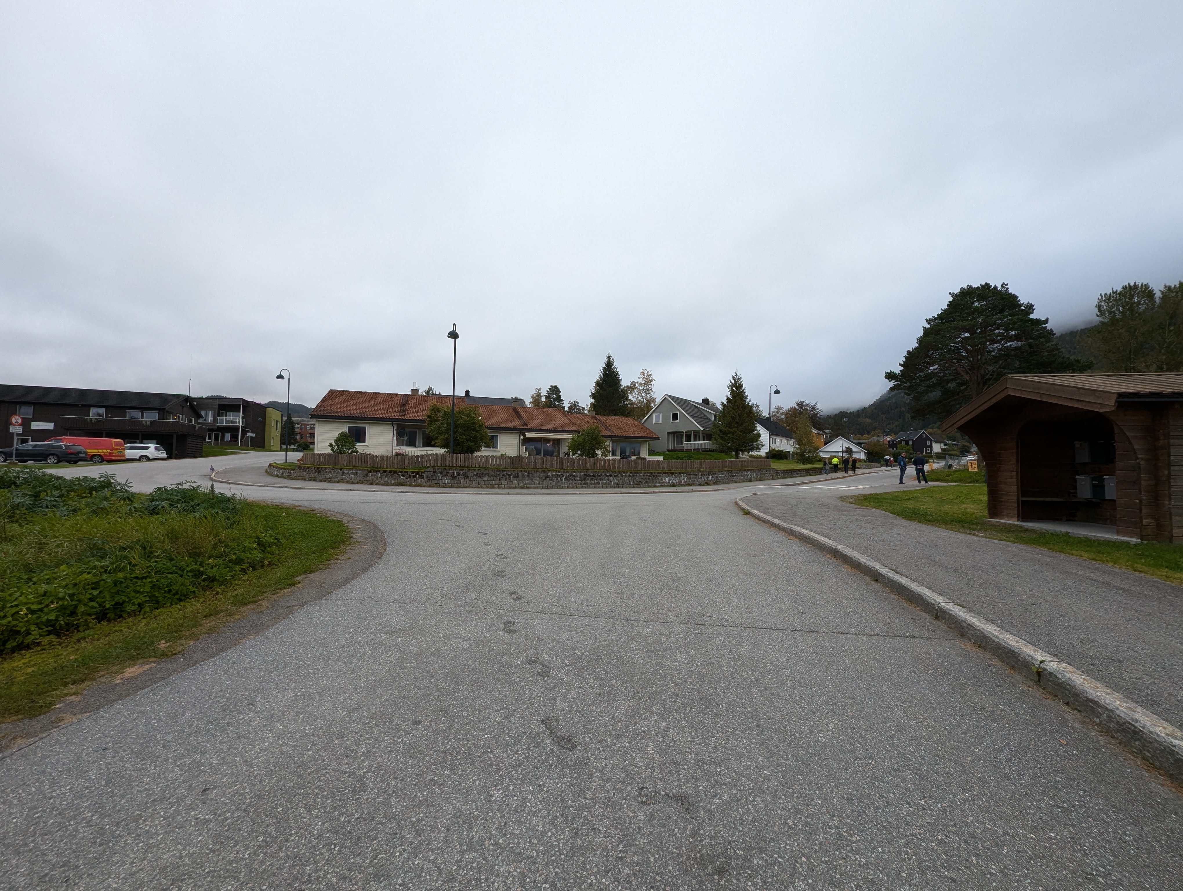 Vi står i ein veg, og ser inn i krysset det er snakk om. Krysset rundar rundt eit hus som ligg midt i. 
