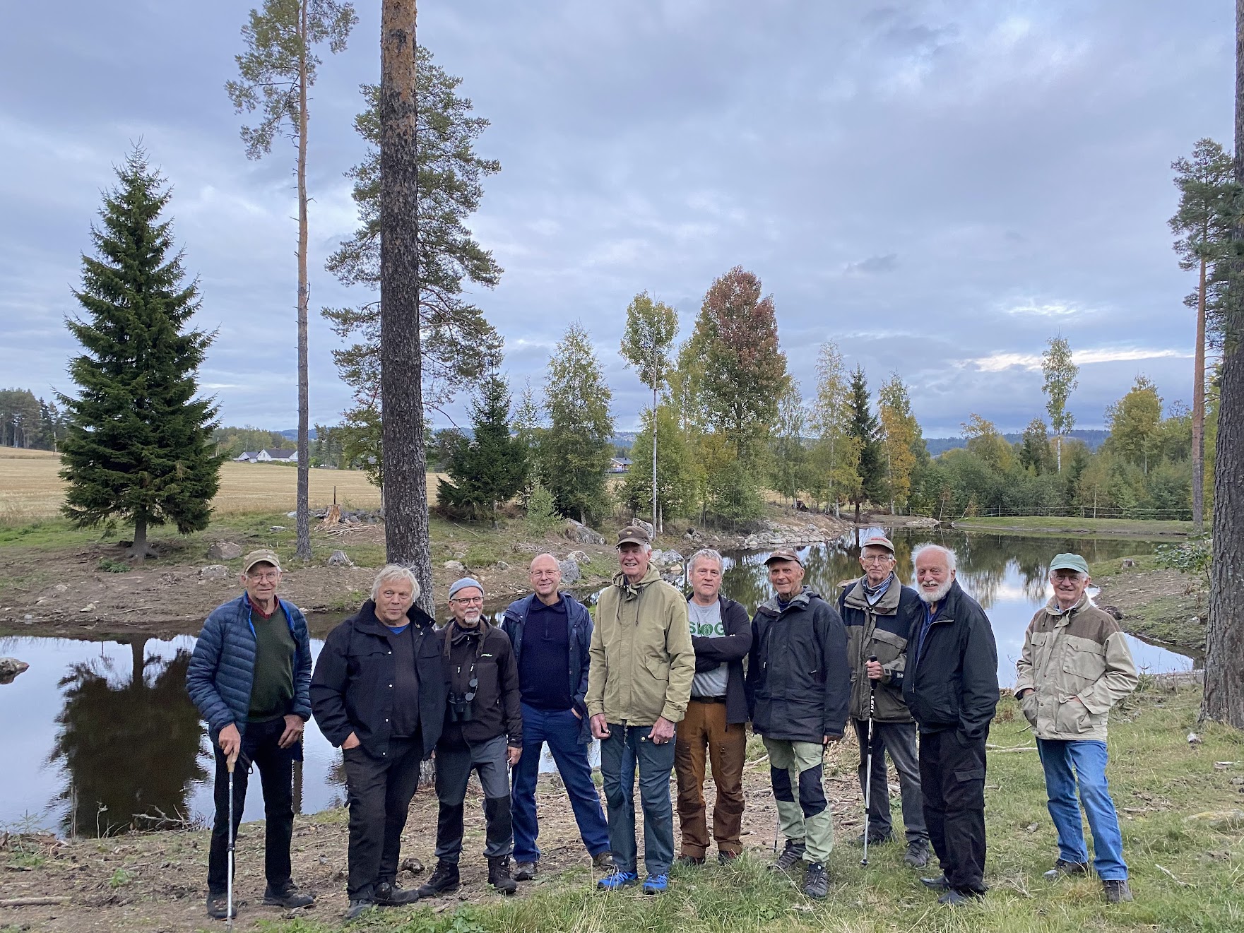 Gruppe med eldre menn står fremfor en dam.