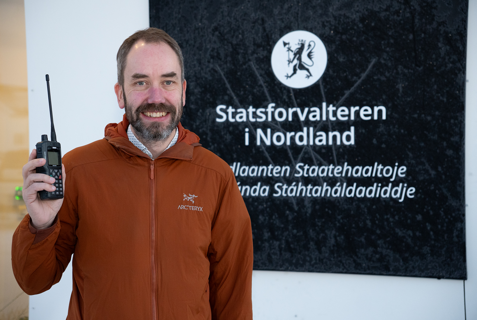 En mann med oransje jakke holder en telefon med antenne.