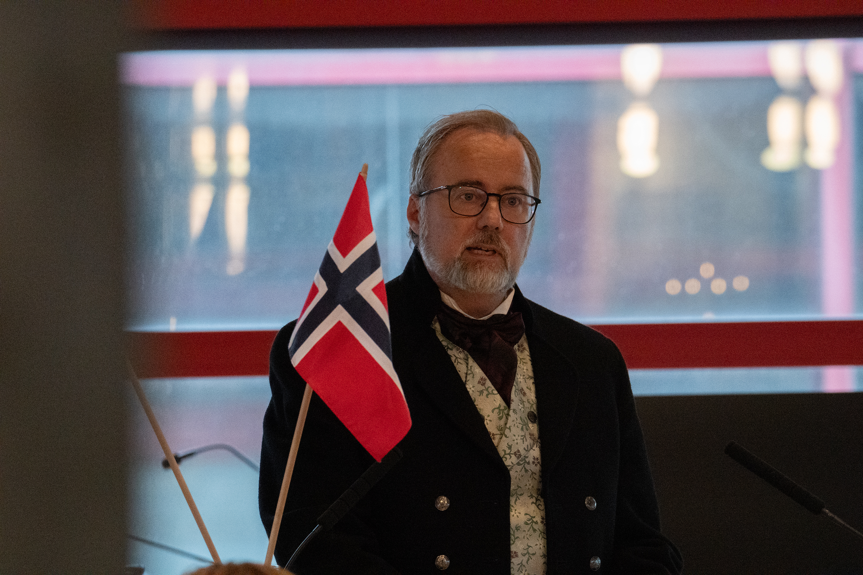 Mann i bunad står bak talerstol.