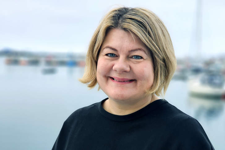 Silje Jakola-Fjeld - ny direktør hos Statsforvalteren i Troms og Finnmark. Smilende kvinne med lyst hår og sort genser. Vann/havn i bakgrunnen. 