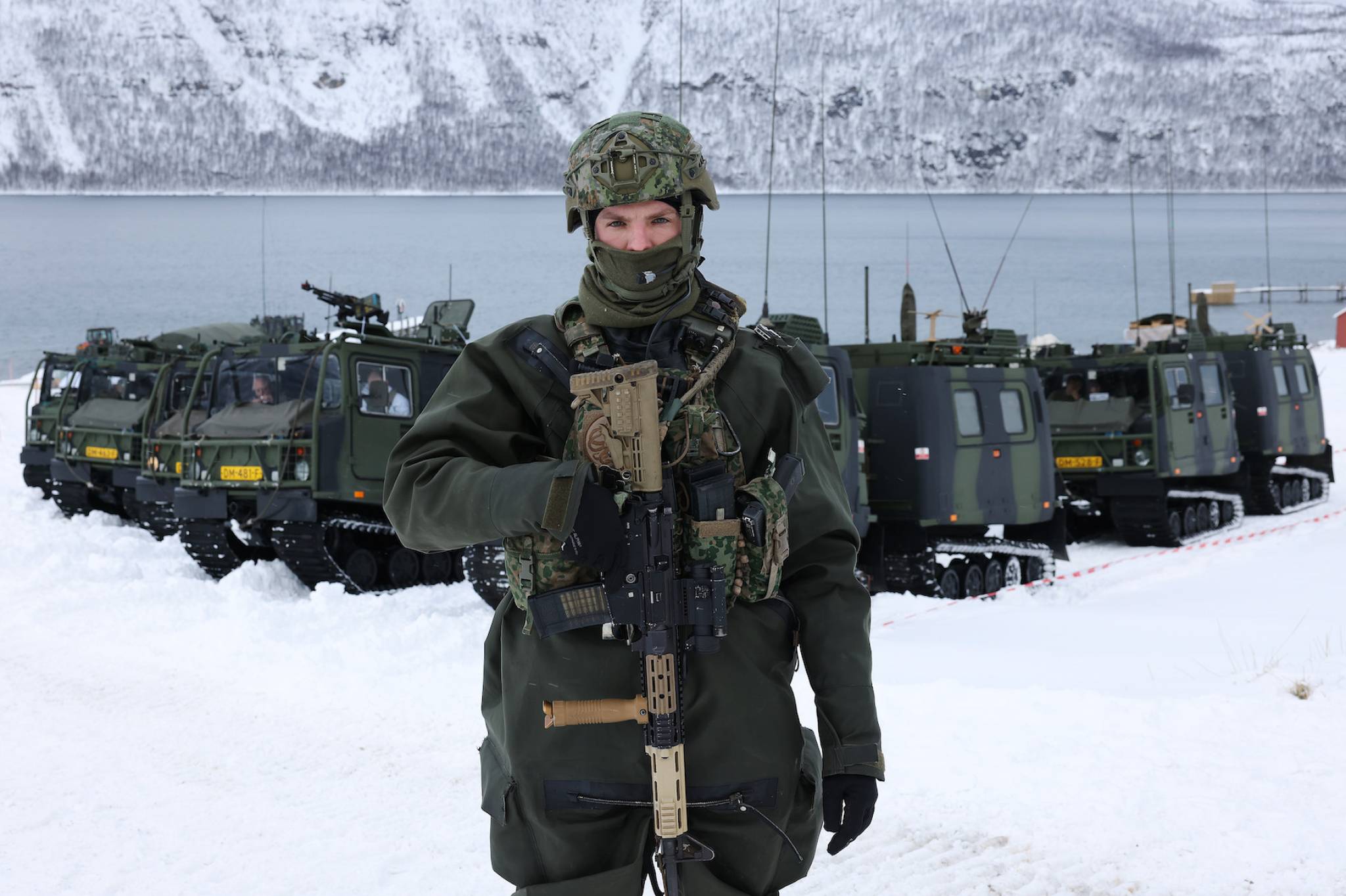 Soldat med uniform og våpen foran beltevogner