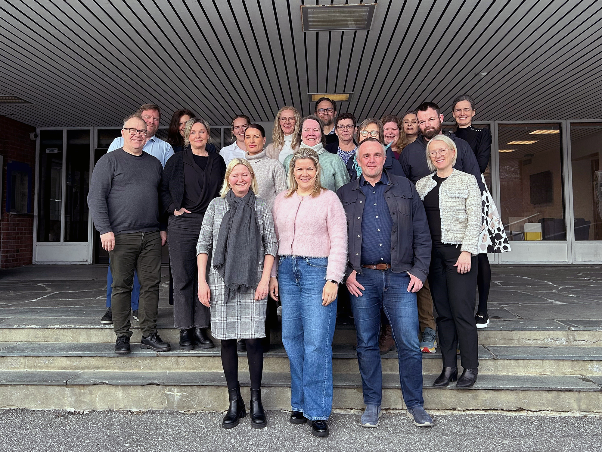 En gruppe mennesker står oppstilt i trapp foran inngangen til et kontorbygg.