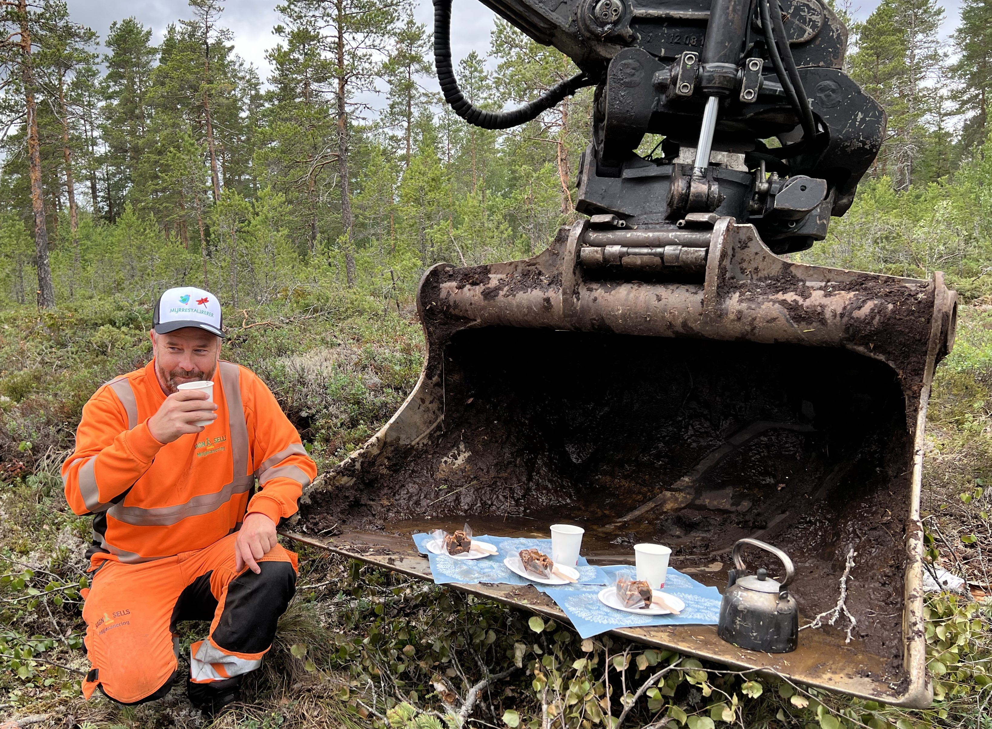 Mann som drikker kaffe ved en anleggsmaskin