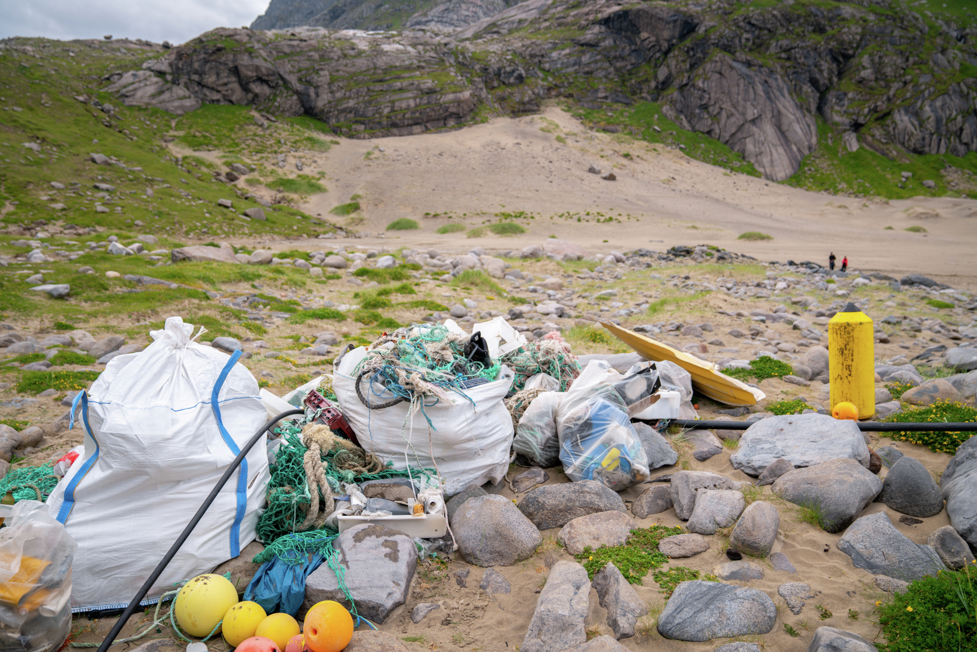 Strand med tau, blåser og annet avfall som har drevet i land og blitt ryddet i hvite søppelsekker, tau.