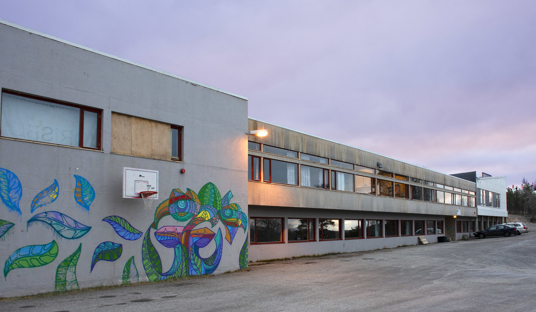 Bildet viser en stor bygning med grå vegger der deler av en vegg er prydet av gatekunst.