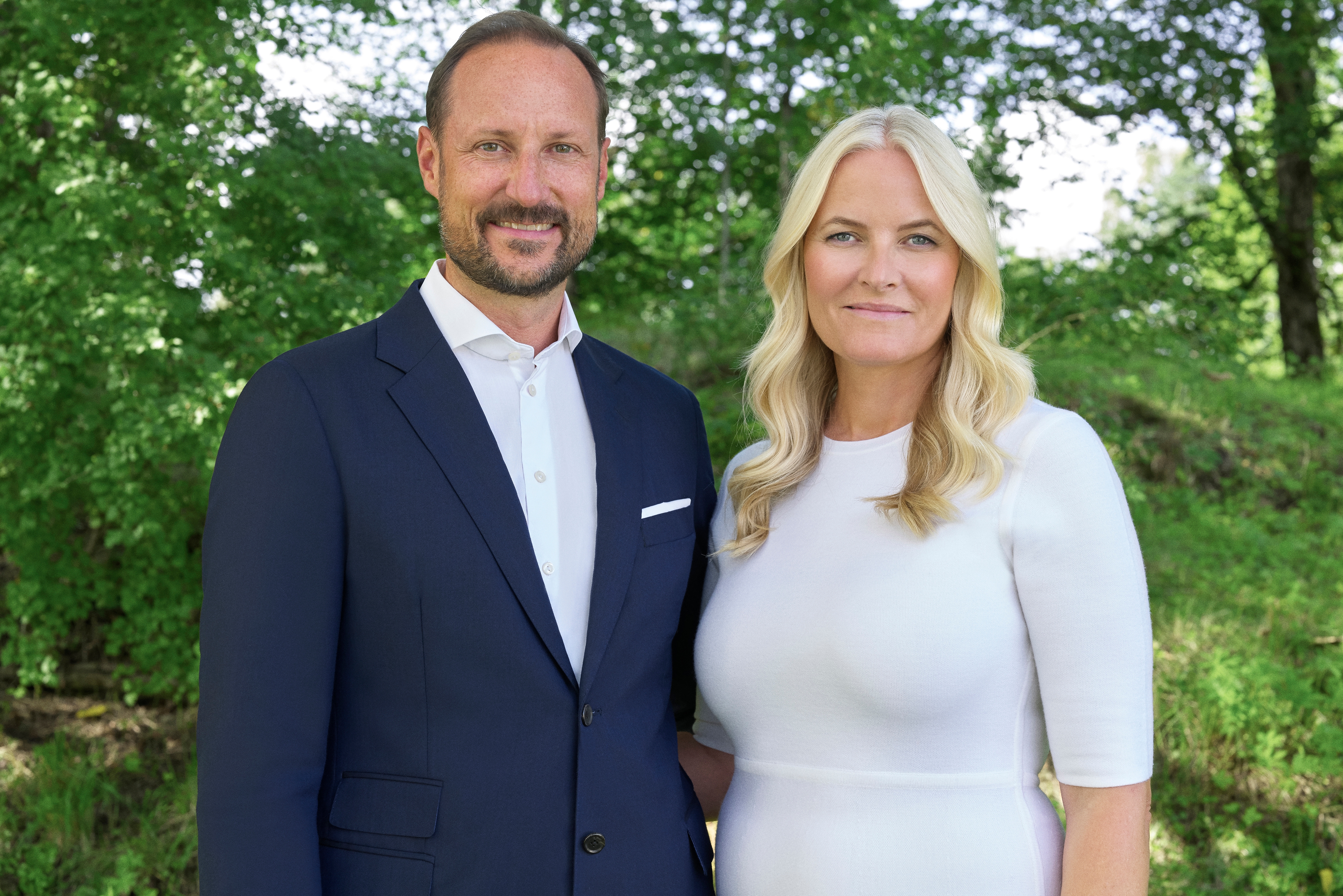 Mann i mørk dress, kvinne i hvit kjole, begge smilende til kamera.