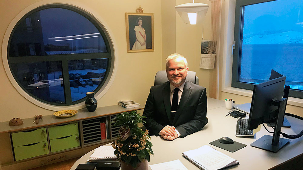 Mann i dress sitter bak skrivebord på kontor.