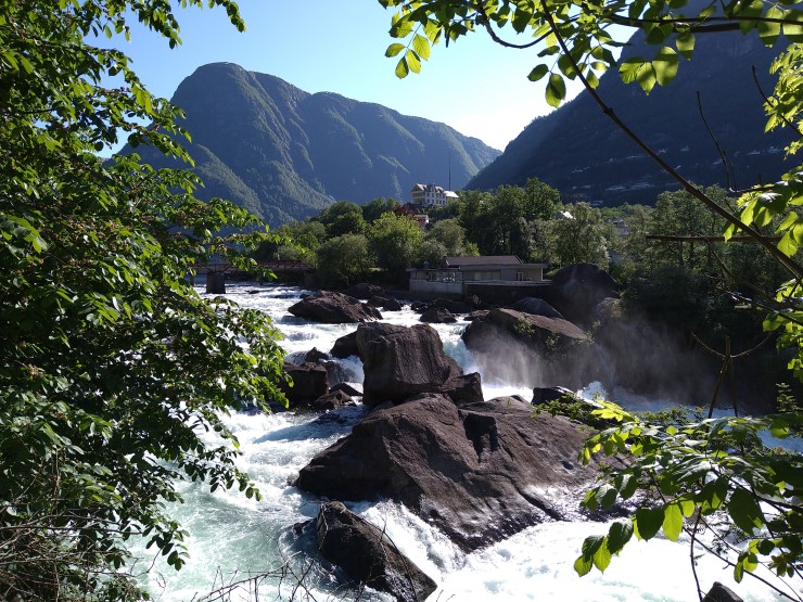Fossande elv som renn kvit mellom store steinar. Bratte fjell i bakgrunn, vestlandsmotiv.