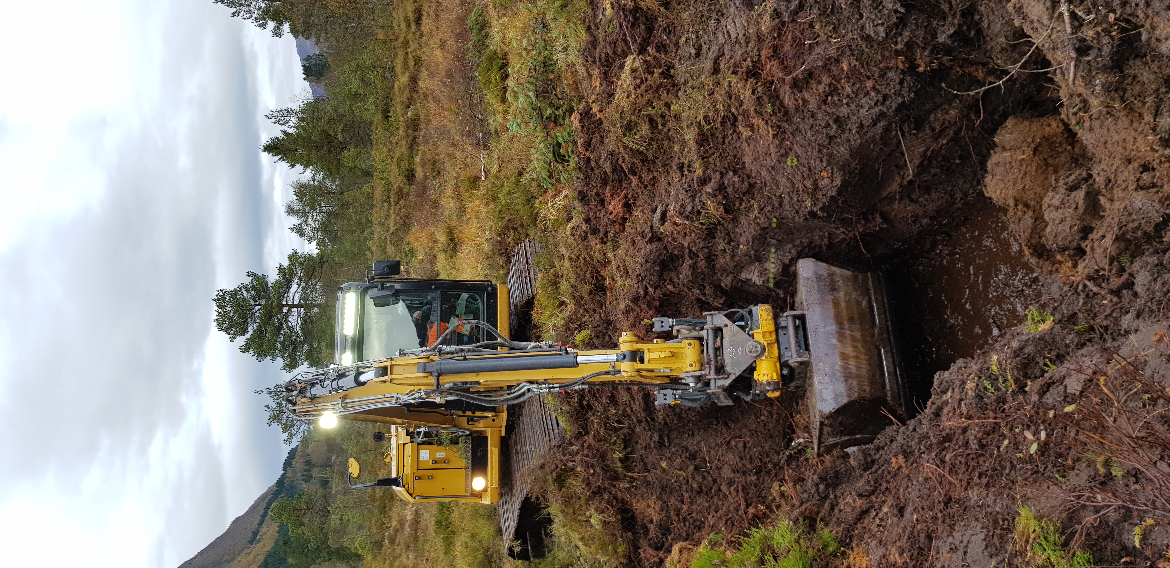 Avskjæring av lekkasje frå høgmyra. Gravemaskin lagar demning for å avskjære lekkasje av vatn frå høgmyra.