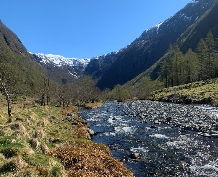 Ei elv gjennom ei dal med fjell i bakgrunnen