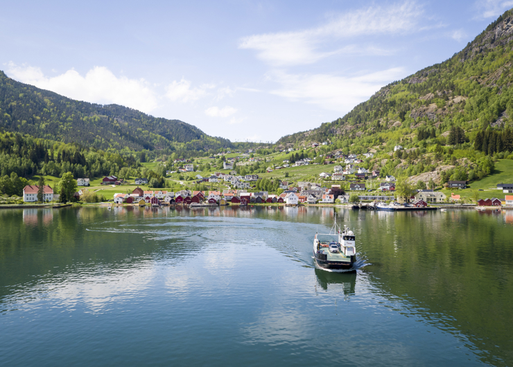 ei ferje kjem mot deg frå ein liten tettstad langs fjorden med blå himmel