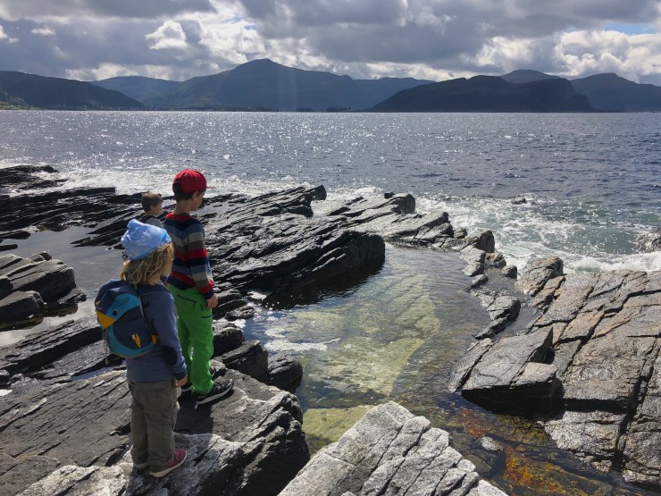 tre barn skuer utover havet med litt fjell i horisonten