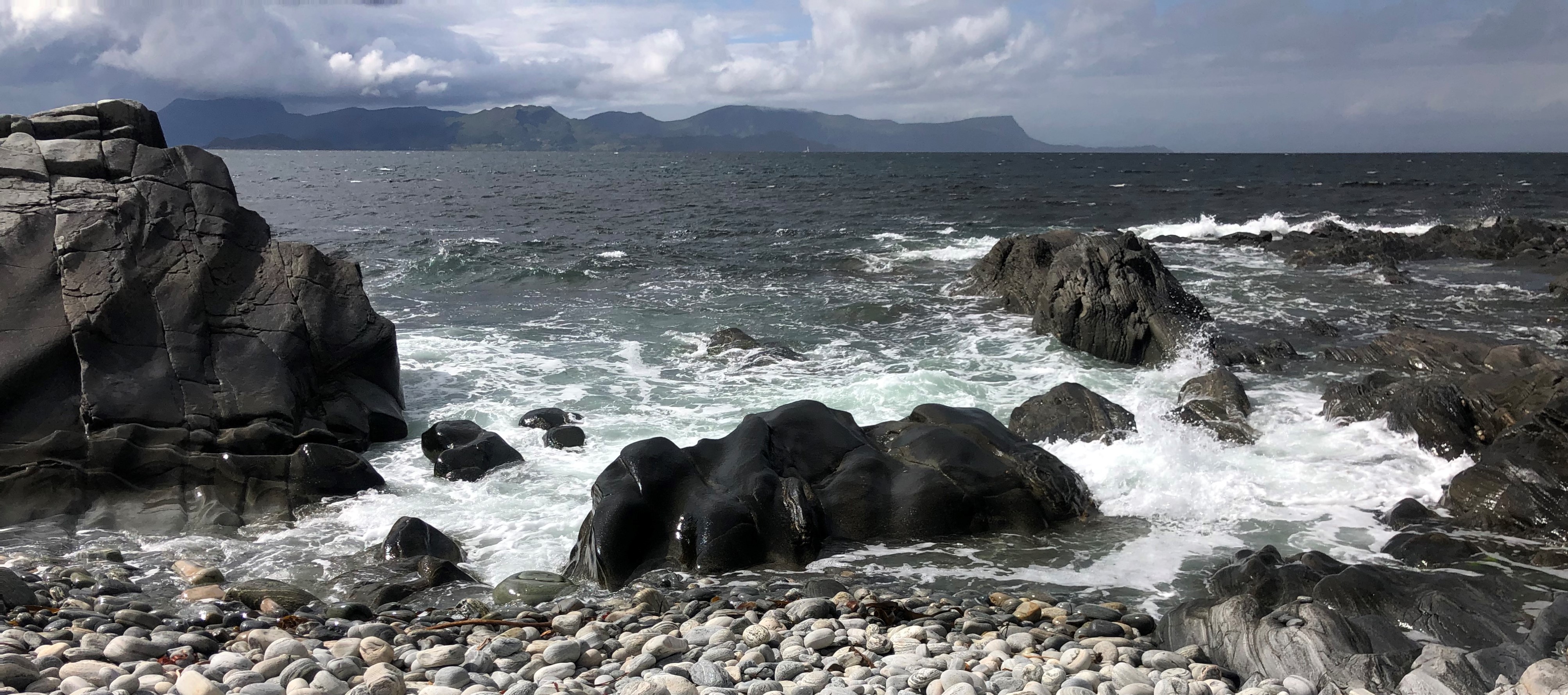 gråvær med bølgjer i havet og steinete strand i forgrunnen
