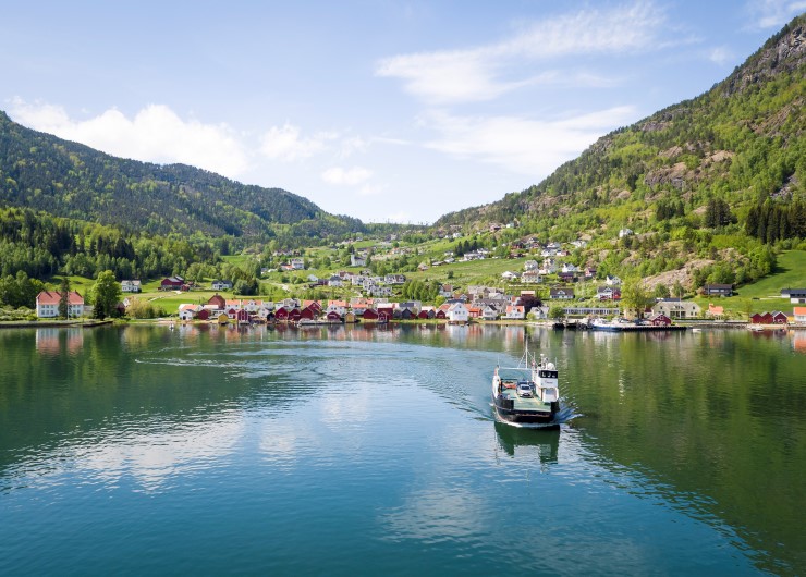 ei ferje med bilar ved ein liten tettstad med kvite hus langs fjorden