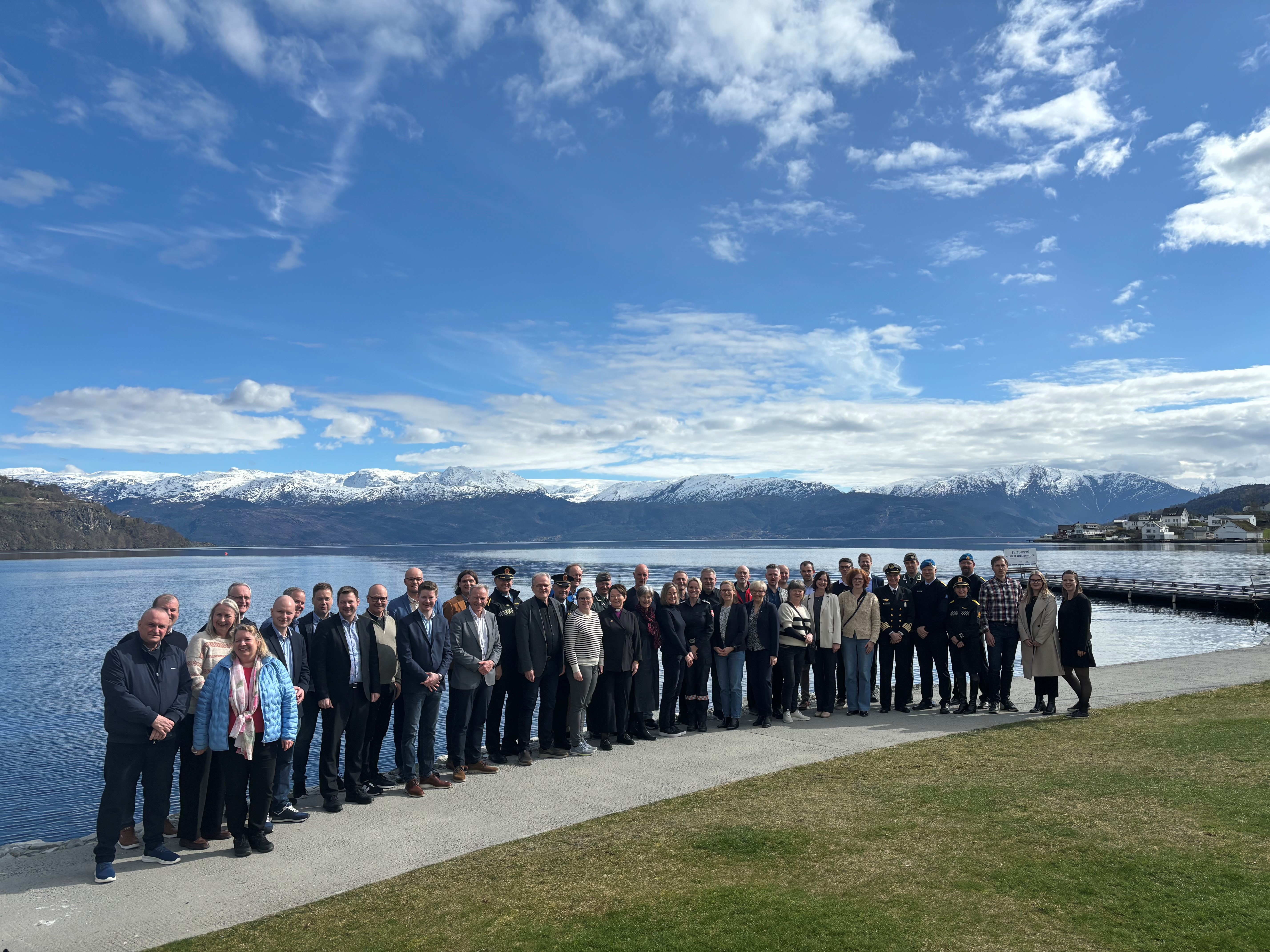 Mange personar oppstilt med fjord og fjell i bakgrunnen. 