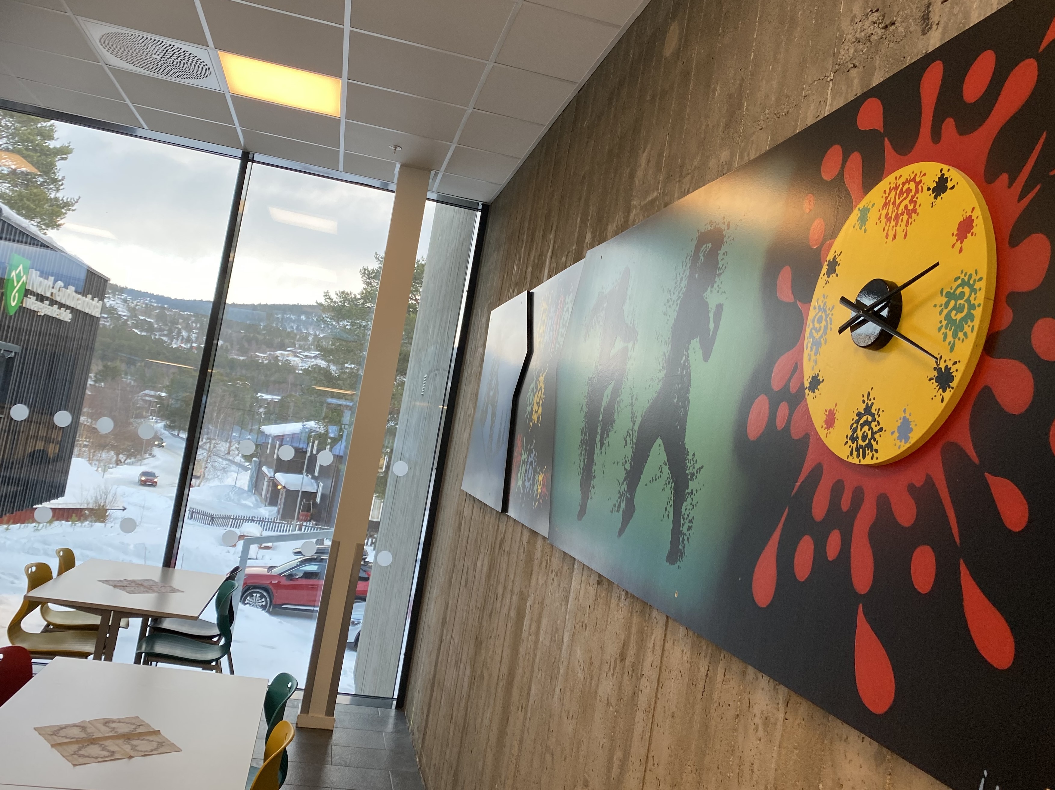 Et fargerikt bilde som henger på veggen på den videregående skolen på Dombås, med fjellene synlig utenfor vinduene.